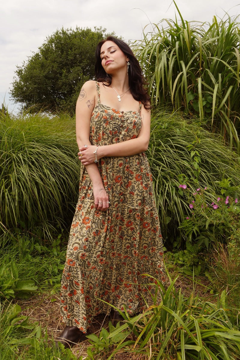 Model wears our Amelia dress as a beautiful loose fit. A full floaty strappy smock style with tiered skirt detailing and a vintage inspired button chest. A lovely wood block style print in a mix of earth 1970s hues by All About Audrey