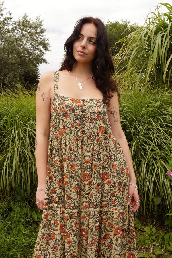 Model wears our Amelia dress as a beautiful loose fit. A full floaty strappy smock style with tiered skirt detailing and a vintage inspired button chest. A lovely wood block style print in a mix of earth 1970s hues by All About Audrey