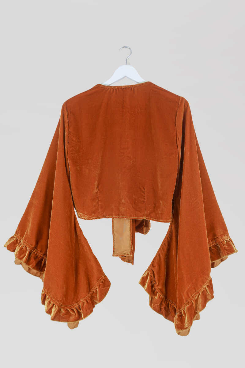 Flat lay of our Velvet Venus Wrap Top in Marmalade Yellow. A dark, warm honey mustard hue in a soft shimmering velvet. Featuring huge bell sleeves with a frill edge. Here it is tied at the front as a tie top inspired by 70's bohemia styles. By All About Audrey