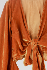 Flat lay of our Velvet Venus Wrap Top in Marmalade Yellow. A dark, warm honey mustard hue in a soft shimmering velvet. Featuring huge bell sleeves with a frill edge. Here it is tied at the front as a tie top inspired by 70's bohemia styles. By All About Audrey